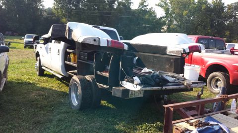 1987 Ford Bronco - A utility truck is parked in a grassy area with a red truck nearby. The utility truck has a large cap on its bed.