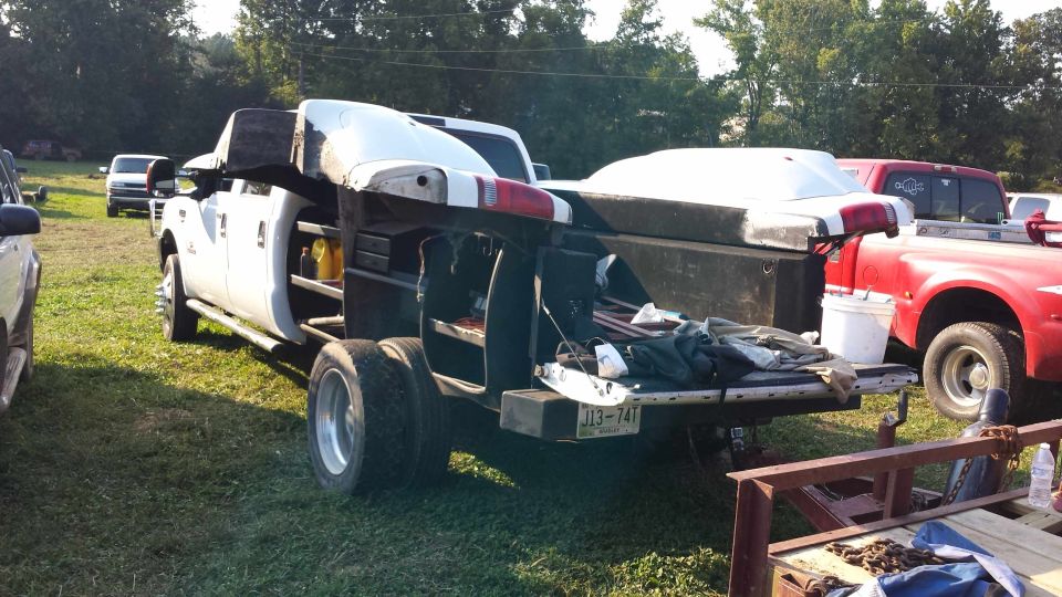 dual rear wheel pickup truck with utility body and a white cap on the bed, parked next to a red pickup truck