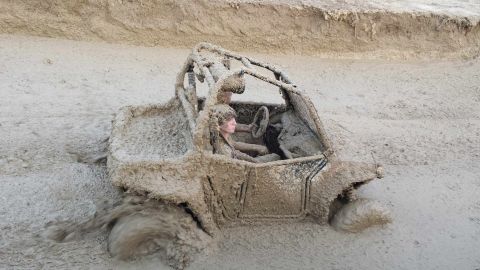 1987 Ford Bronco - An off-road vehicle is deeply stuck in mud, with a person visible in the driver's seat.