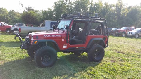 1987 Ford Bronco - A red Jeep Wrangler is parked in a field with several other vehicles visible in the background.