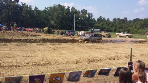 1987 Ford Bronco - Off-road vehicles compete in a mud pit event, with spectators watching from the sidelines.