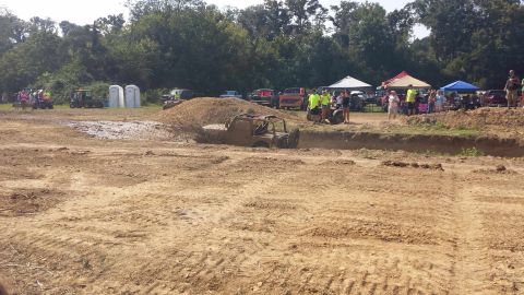 1987 Ford Bronco - An off-road vehicle is stuck in a mud pit during an event, with spectators gathered in the background.