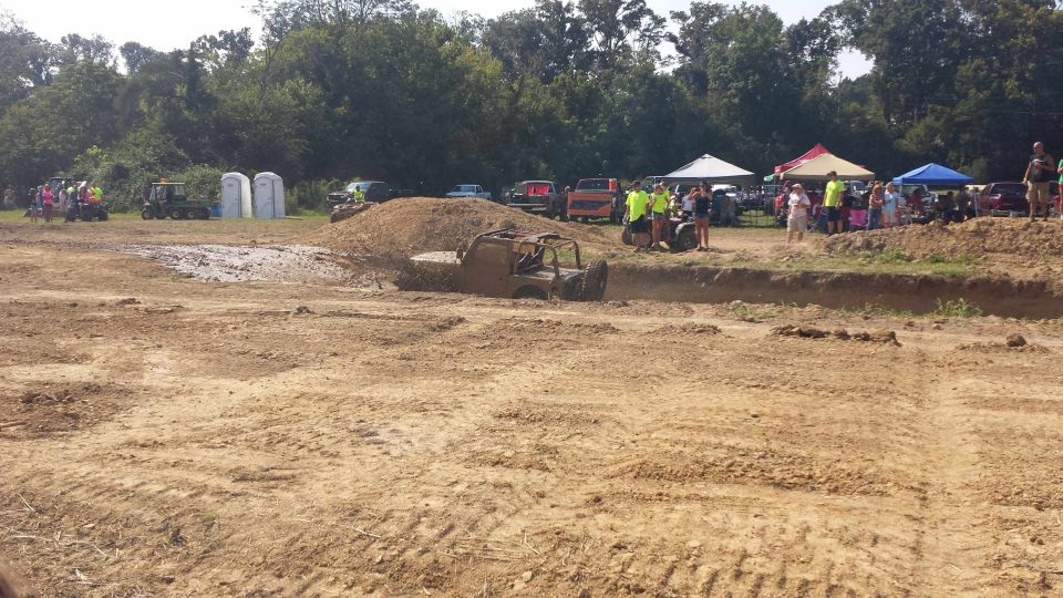 off-road vehicle stuck in mud pit with spectators watching