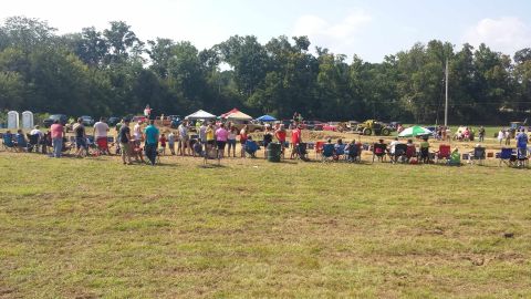 1987 Ford Bronco - An outdoor gathering features spectators seated in chairs, with various vehicles visible in the distance.