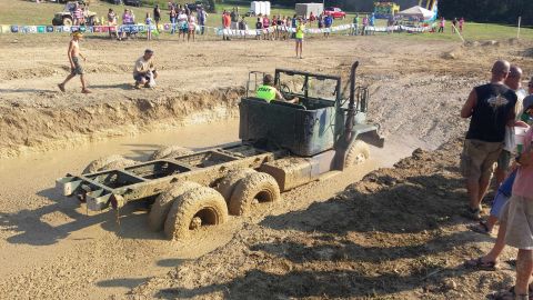 1987 Ford Bronco - This military truck chassis is stuck in a mud pit during an event. A person in a 'STAFF' shirt is driving.