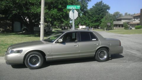 2000 Mercury Grand Marquis - Side view of a gold 2000 Mercury Grand Marquis sedan parked on a residential street.