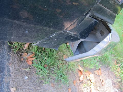 2001 Ford Crown Victoria - The rear bumper corner of a 2001 Ford Crown Victoria is visible, with grass and fallen leaves on the ground.
