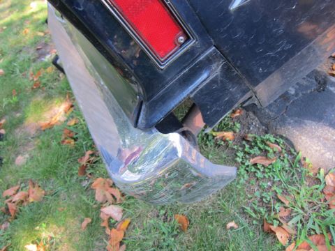 2001 Ford Crown Victoria - Close-up of a chrome rear bumper and part of a black car's body with a red taillight.