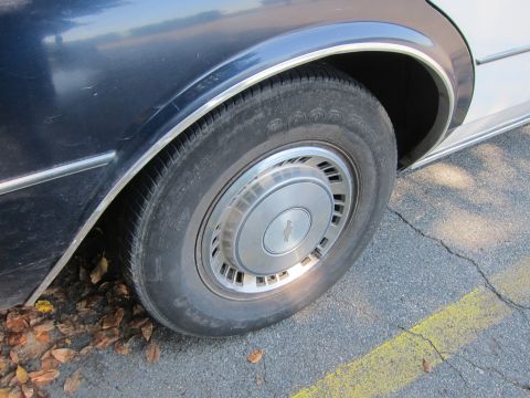2001 Ford Crown Victoria - Side view of a car's wheel and fender, showing chrome trim and a hubcap with a Chevrolet logo.