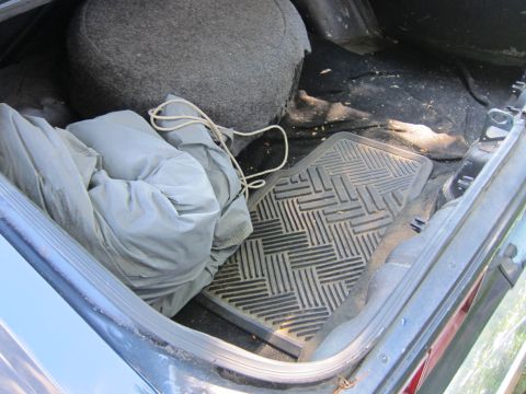 2001 Ford Crown Victoria - The interior of a car trunk shows a folded car cover and a rubber floor mat.
