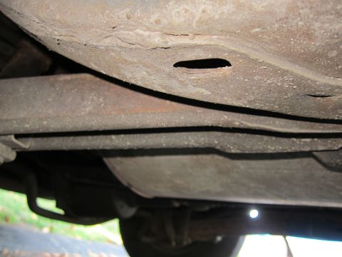 2001 Ford Crown Victoria - The underside of a vehicle shows significant rust and a hole in the frame, indicating potential structural wear.