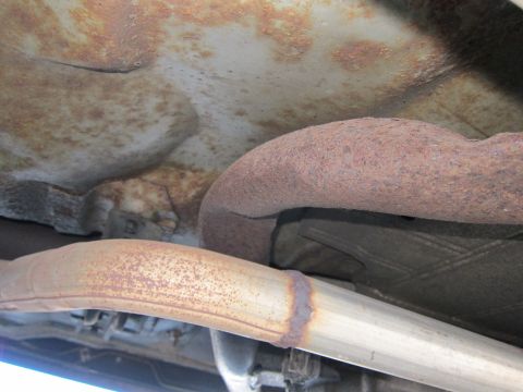 2001 Ford Crown Victoria - Close-up view of heavily rusted exhaust pipes underneath a vehicle.