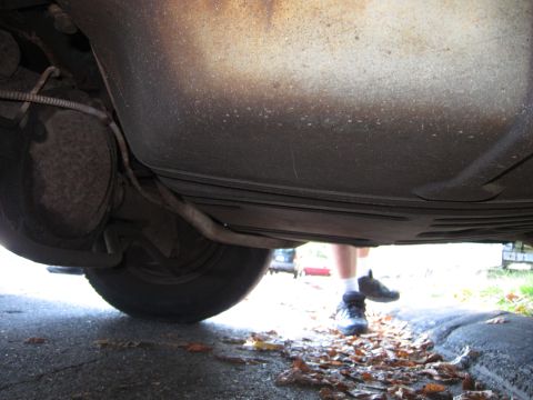 2001 Ford Crown Victoria - A low-angle shot reveals the undercarriage of a vehicle, including the exhaust system and a rear wheel, with a person's legs visible in the…