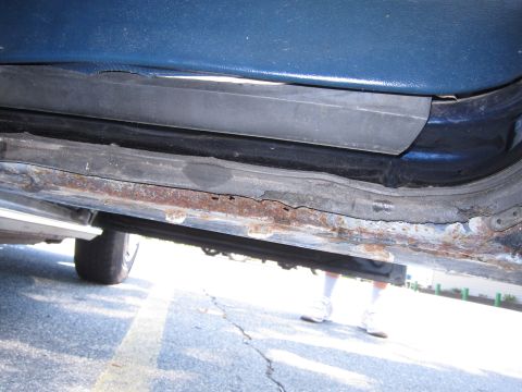2001 Ford Crown Victoria - The underside of a blue vehicle shows significant rust on the rocker panel and door sill area.