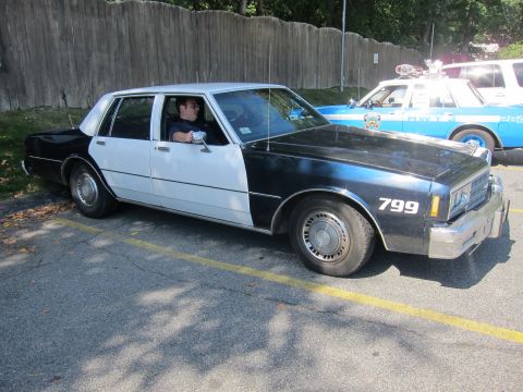 2001 Ford Crown Victoria - A two-tone police car is parked next to a blue and white police vehicle.