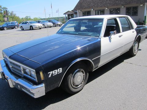 2001 Ford Crown Victoria - This police car, marked with '799', is a dark blue and white sedan with a chrome bumper and hubcaps.