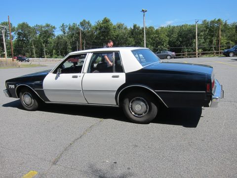 2001 Ford Crown Victoria - A two-tone black and white police car is parked in a lot on a sunny day.