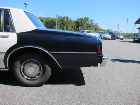 2001 Ford Crown Victoria - Side view of a two-tone police car's rear section, with other vehicles in the background.