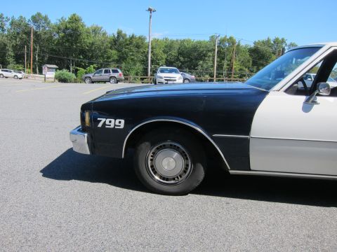 2001 Ford Crown Victoria - A two-tone police car, dark blue and white, is parked in a lot with other vehicles.