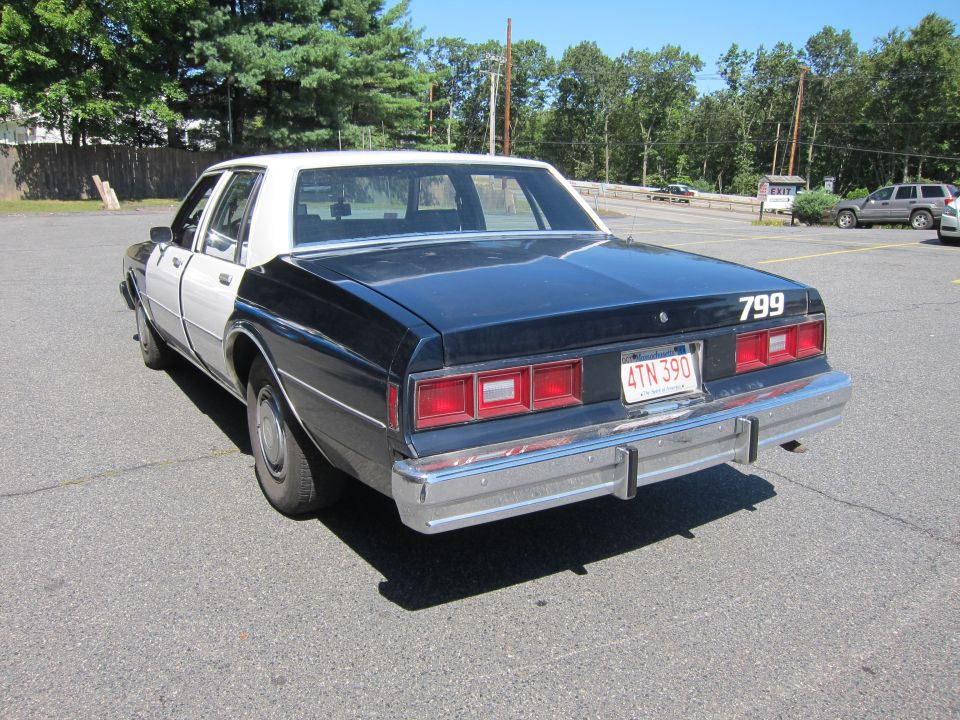 Police car with black and white paint, rear view, showing "799" on trunk and Massachusetts license plate "4TN 390"