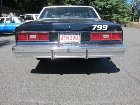 2001 Ford Crown Victoria - A black sedan with a white roof and the number 799 displayed on the trunk is seen from the rear, with another police vehicle visible to the…