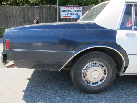 2001 Ford Crown Victoria - A two-tone police car is parked near a sign for Tony's Pizza, indicating additional parking and entrances.
