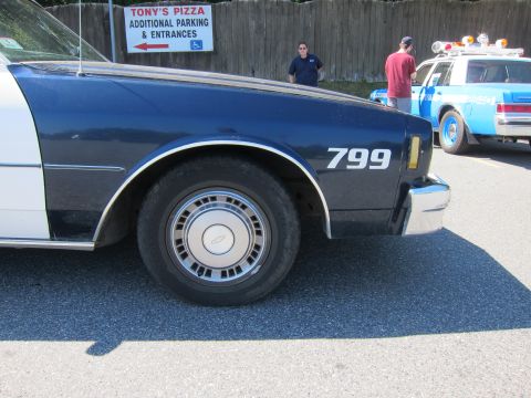 2001 Ford Crown Victoria - A dark blue and white police car, marked with the number 799 on its fender, is parked next to another police vehicle.