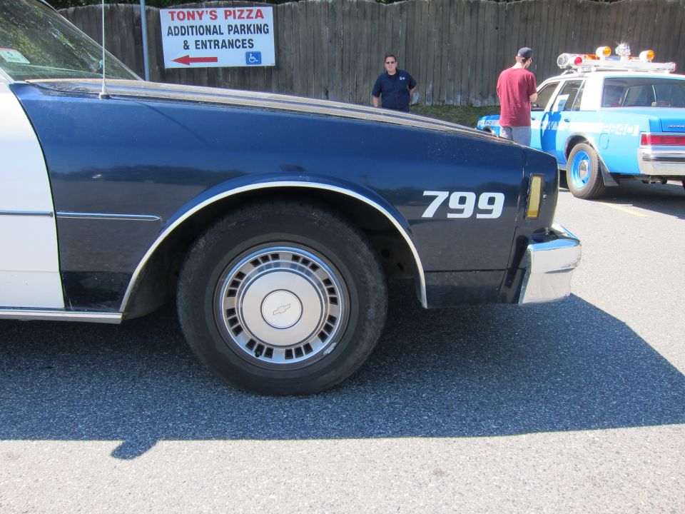 Police car fender with number 799, showing part of wheel and chrome bumper