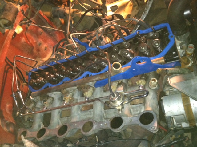 Close-up of engine valve cover with blue gasket and intake manifold components