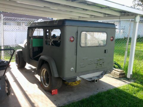 Jeep CJ-8 Scrambler parked under a carport, rear view. It has a hardtop and is painted olive drab