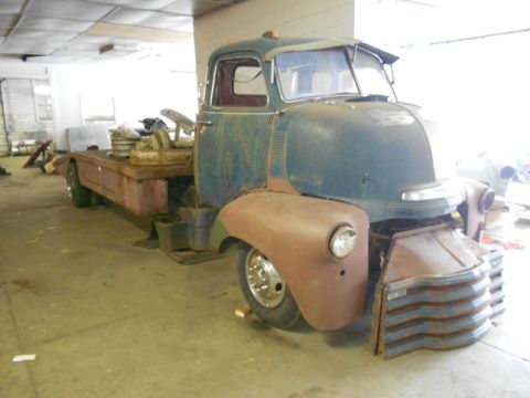Front view of a rusty blue and brown tow truck with a flatbed
