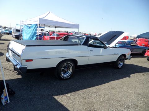 1973 Ford Ranchero - A white Ford Ranchero is parked at an outdoor event with its hood up, surrounded by other vehicles and tents.