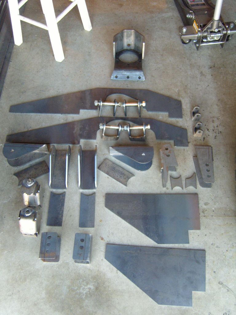 Unpainted steel brackets, shackles, and plates for a Jeep build laid out on a garage floor