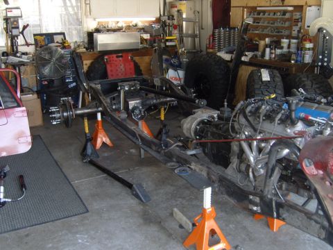 1985 Jeep CJ7 - The chassis of a Jeep CJ is shown on jack stands, with the engine and drivetrain components visible.