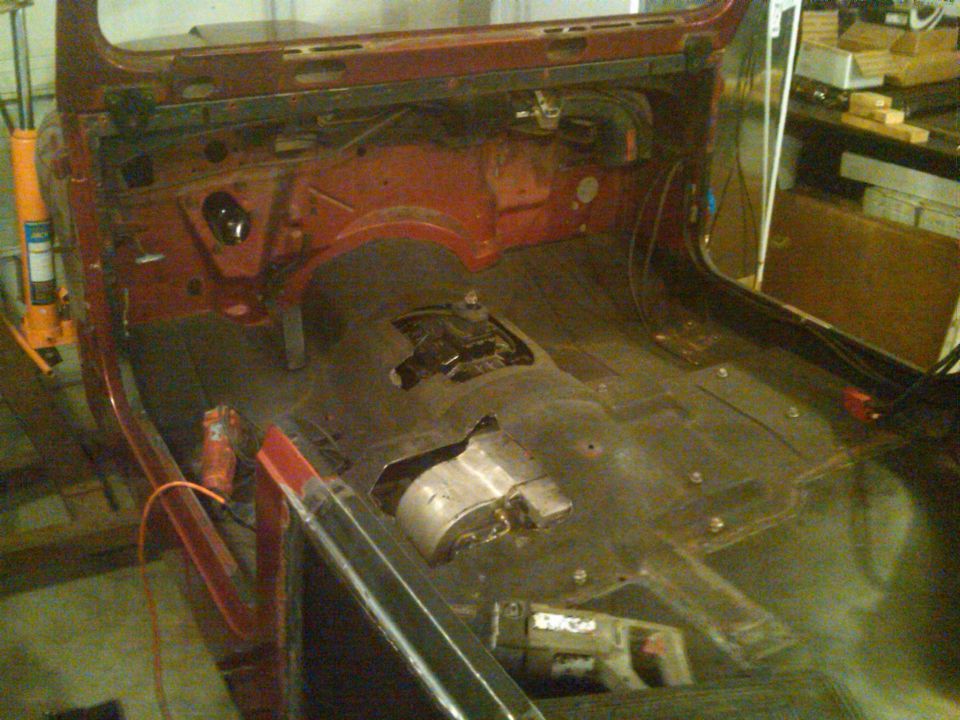 Interior of a red Jeep CJ7, stripped down for restoration, showing the floor pan and transmission tunnel