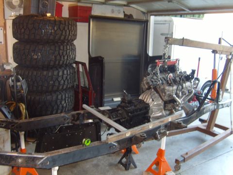 1985 Jeep CJ7 - Engine and transmission assembly being installed onto a vehicle frame in a garage setting.