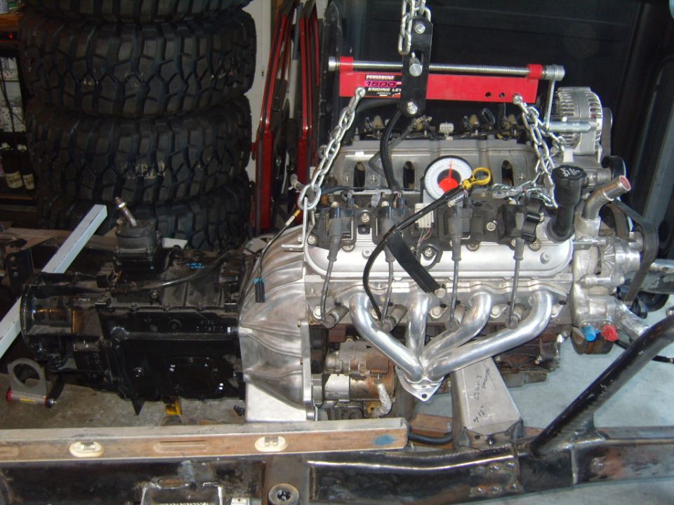 Engine and transmission assembly suspended by a red engine hoist, with exhaust headers attached