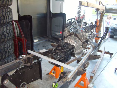1985 Jeep CJ7 - Engine and transmission assembly being worked on, with a stack of tires and a partial vehicle body in the background.