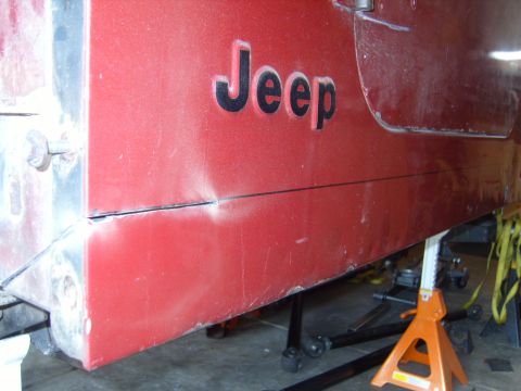 1985 Jeep CJ7 - Close-up of a red 1985 Jeep CJ7 side panel, showing the 'Jeep' lettering and a dent.