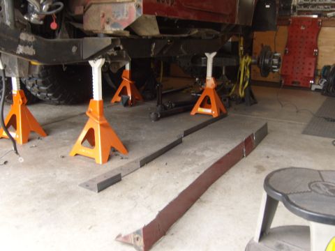 1985 Jeep CJ7 - The underside of a Jeep is supported by multiple jack stands in a garage setting.