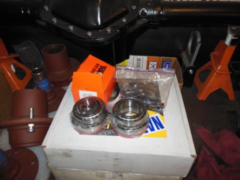 1985 Jeep CJ7 - Various automotive parts, including a differential and new bearings, are laid out on a surface with support stands nearby.