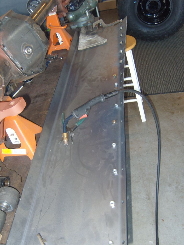 Sheet metal panel with pre-drilled holes and a welding gun, on sawhorses with a tire in the background