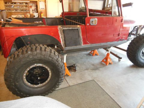 1985 Jeep CJ7 - This red Jeep CJ-series is in a garage, supported by jack stands, with visible custom body modifications and oversized tires.