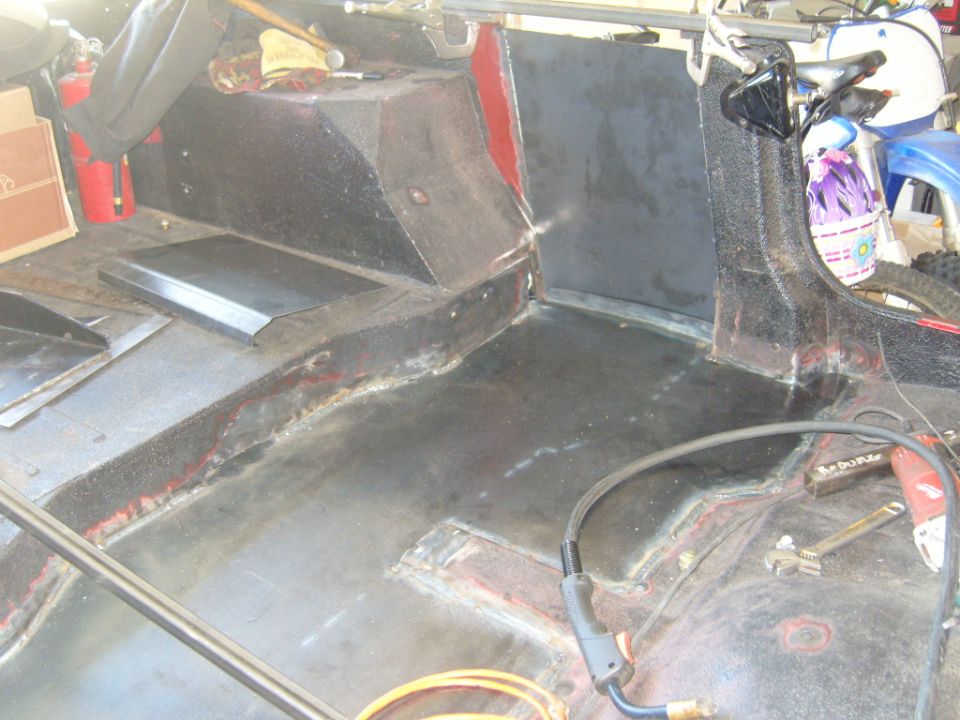 Interior of a Jeep being worked on, showing floor and rear panels. Fire extinguisher and tools are visible