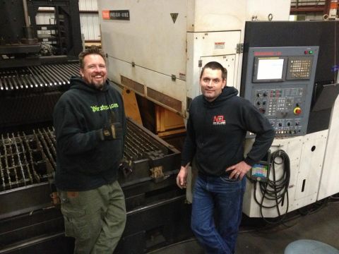1985 Jeep CJ7 - Two men pose in front of complex machinery in what appears to be a workshop or factory setting.
