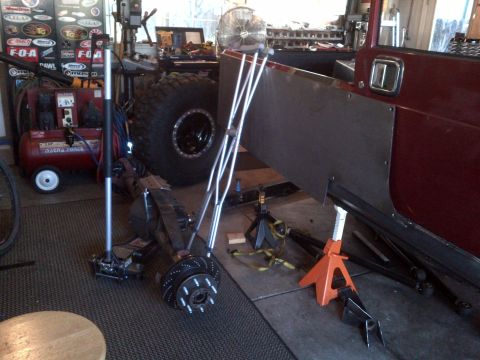 1985 Jeep CJ7 - A red Jeep CJ-series body is undergoing modifications in a workshop, custom metal panels and a large off-road tire.
