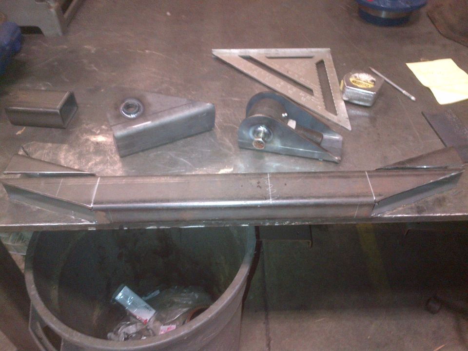 Metal fabrication parts on a workbench with a square and tape measure