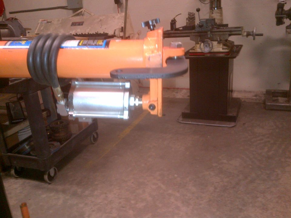Orange hydraulic cylinder with black hose on a wheeled cart, in a workshop setting