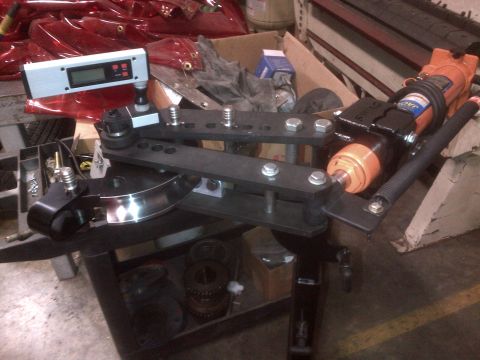 1985 Jeep CJ7 - A tube bender is shown with various metal parts and tools in a workshop setting.