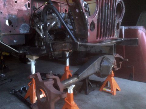 1985 Jeep CJ7 - The front end of a Jeep CJ is elevated on jack stands, showing the frame, engine, and suspension components.